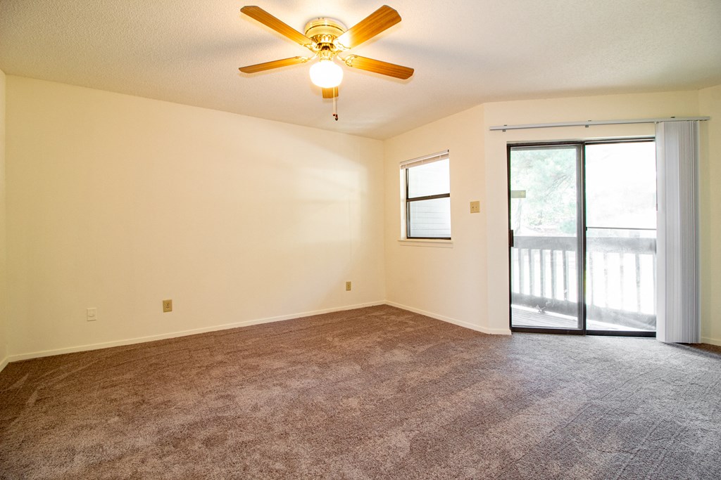 an empty living room with a ceiling fan and a sliding glass door
