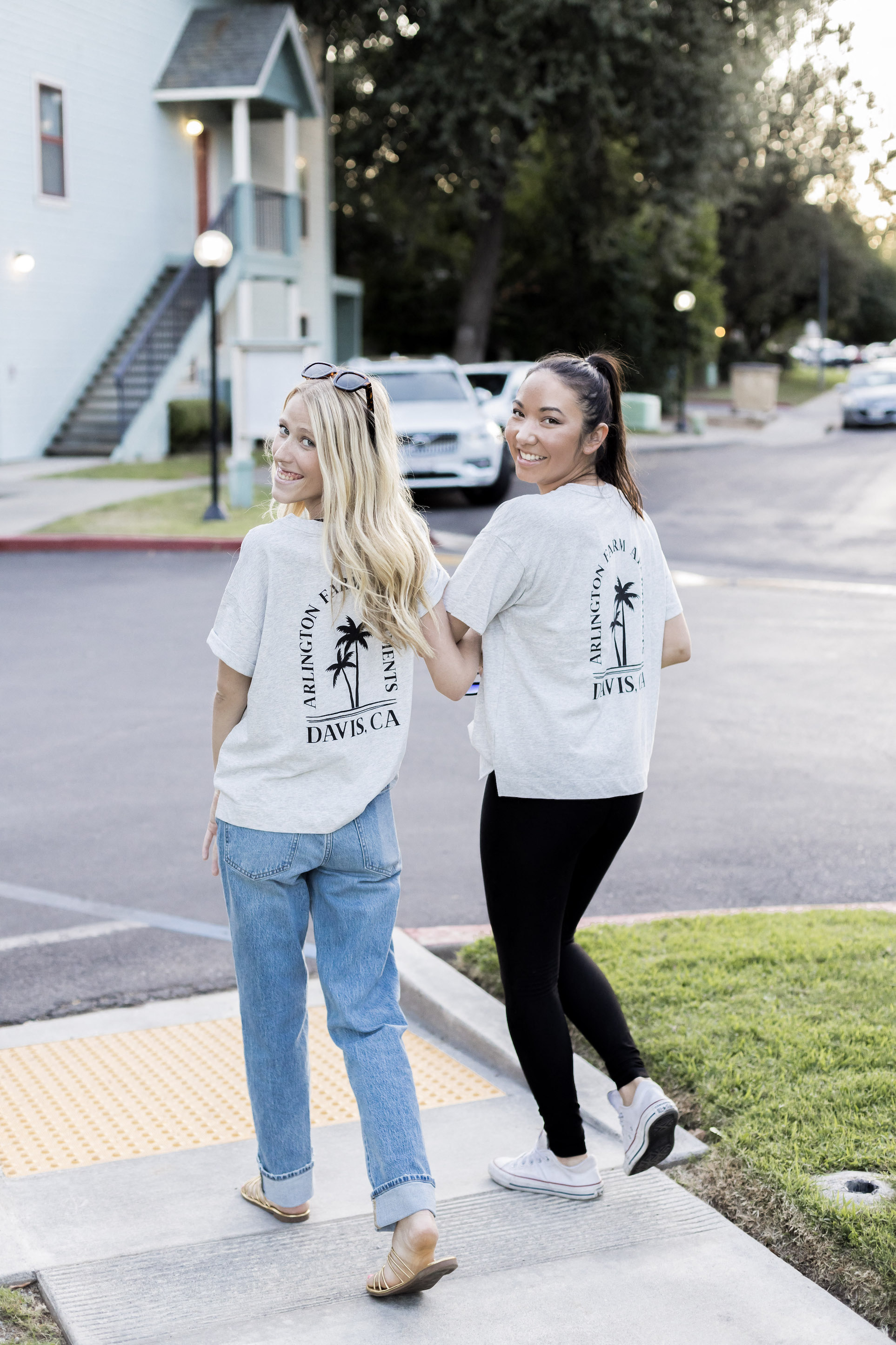 Two young women walking arm in arm, smiling looking back at the camera