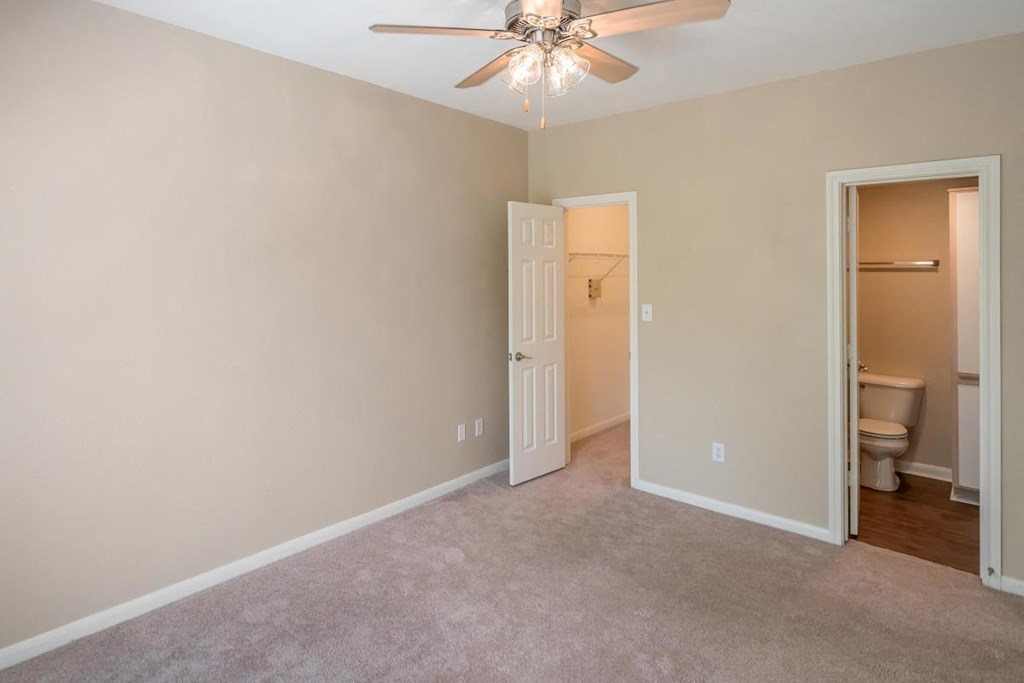 a bedroom with a ceiling fan and a door to a bathroom