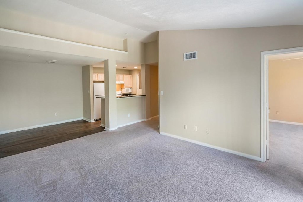 an empty living room with a kitchen in the background