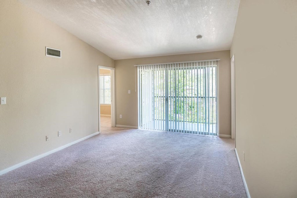 an empty living room with a sliding glass door to a balcony