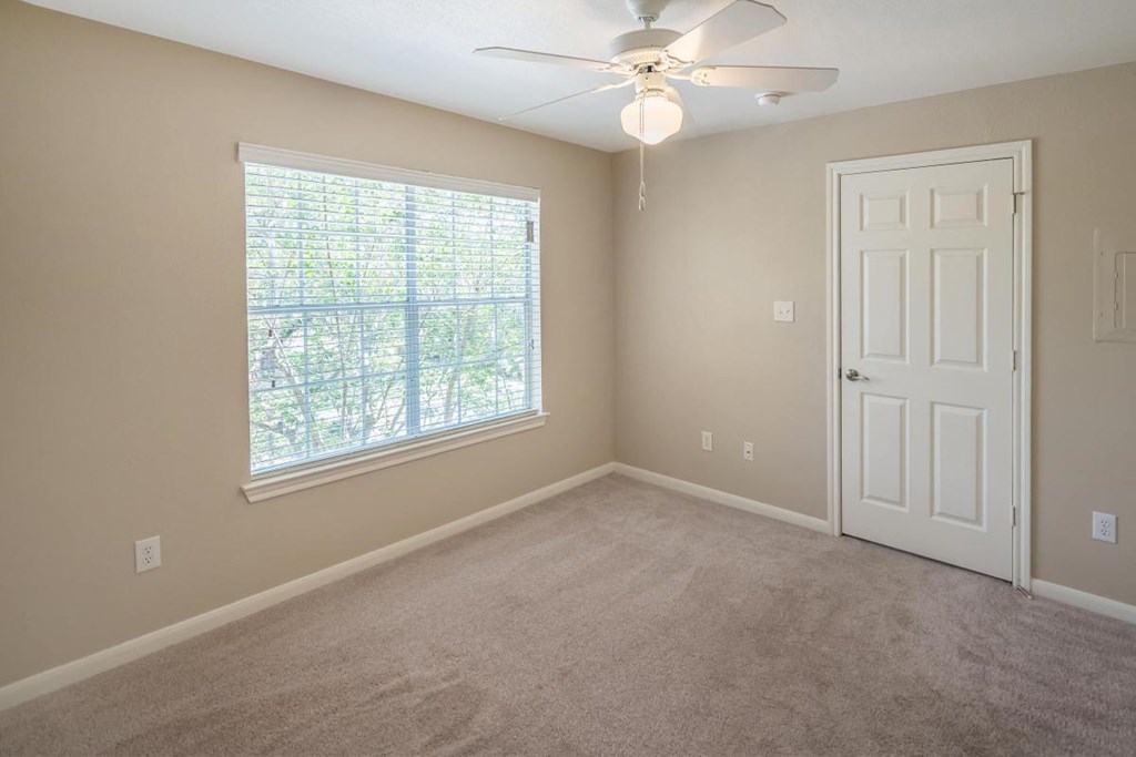 an empty bedroom with a ceiling fan and a window