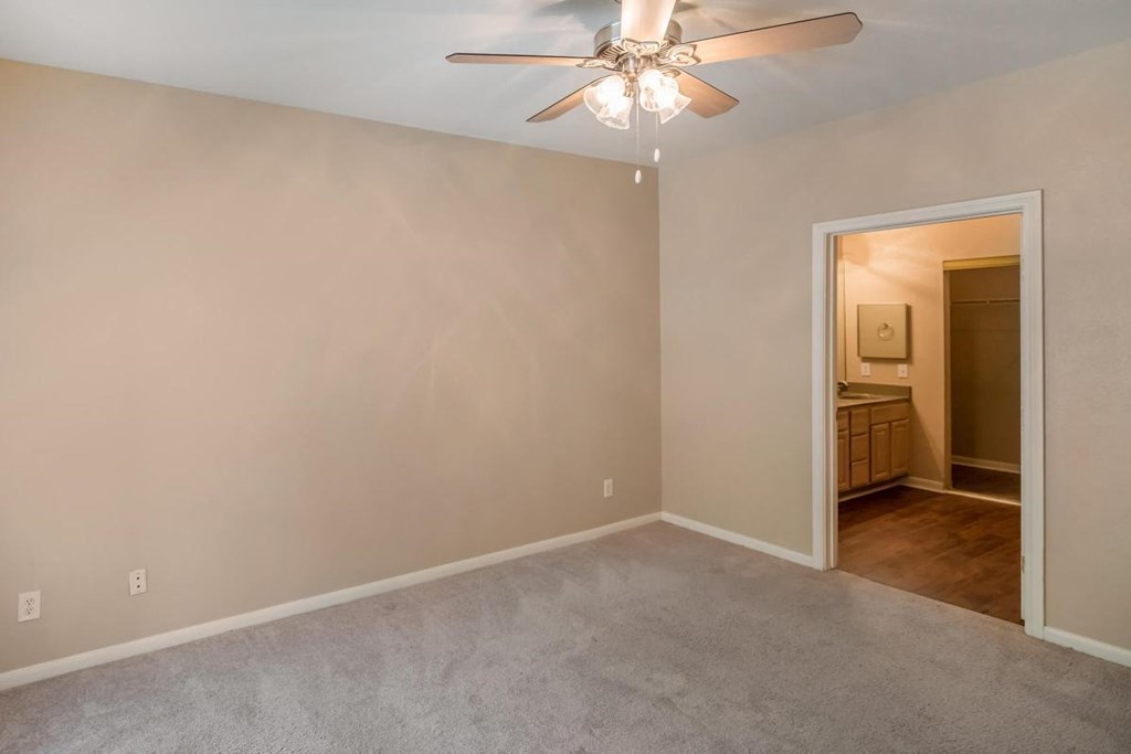 an empty living room with a ceiling fan and a door to a bathroom