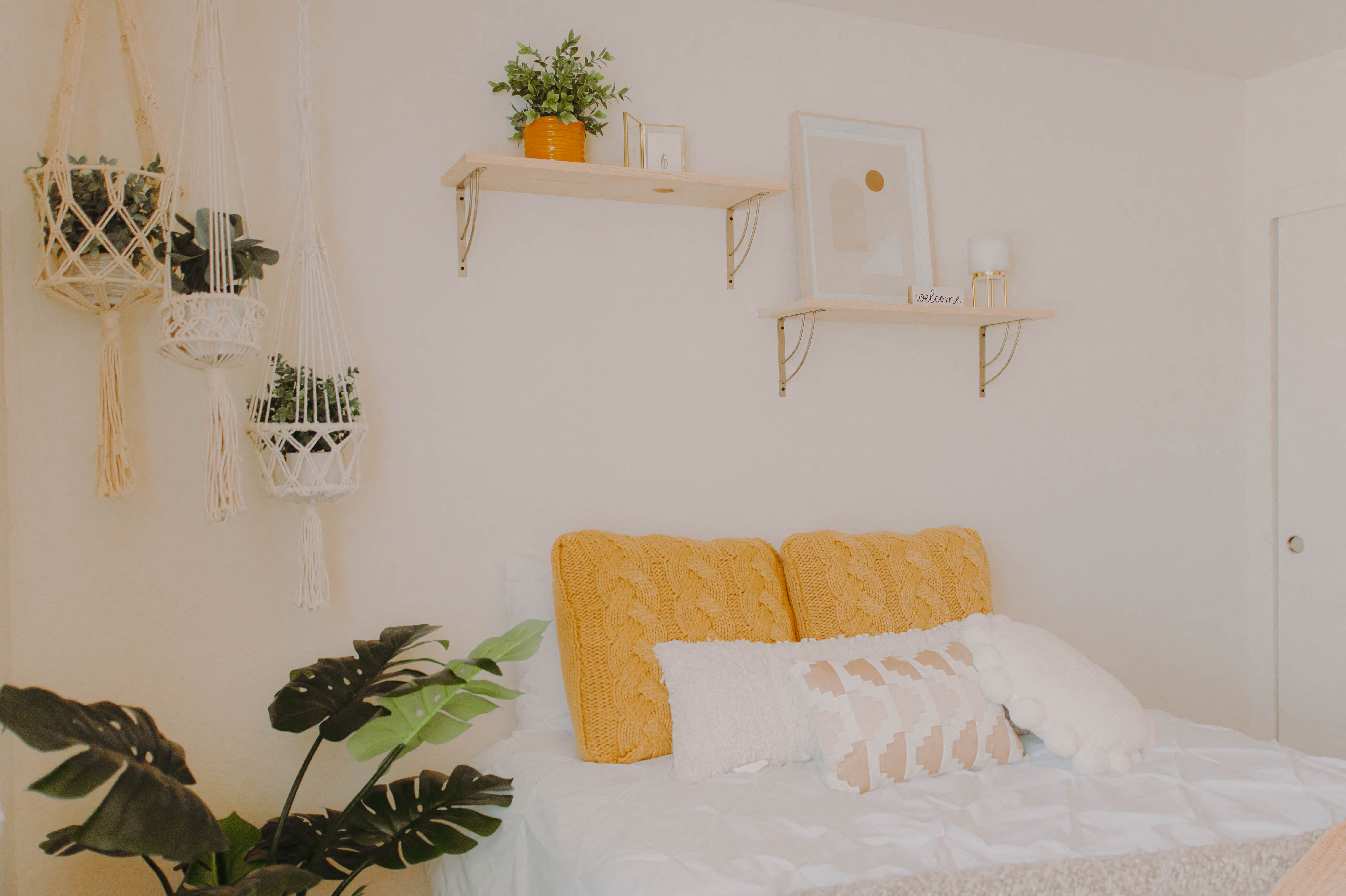 a white bedroom with a bed with white and yellow pillows and plants