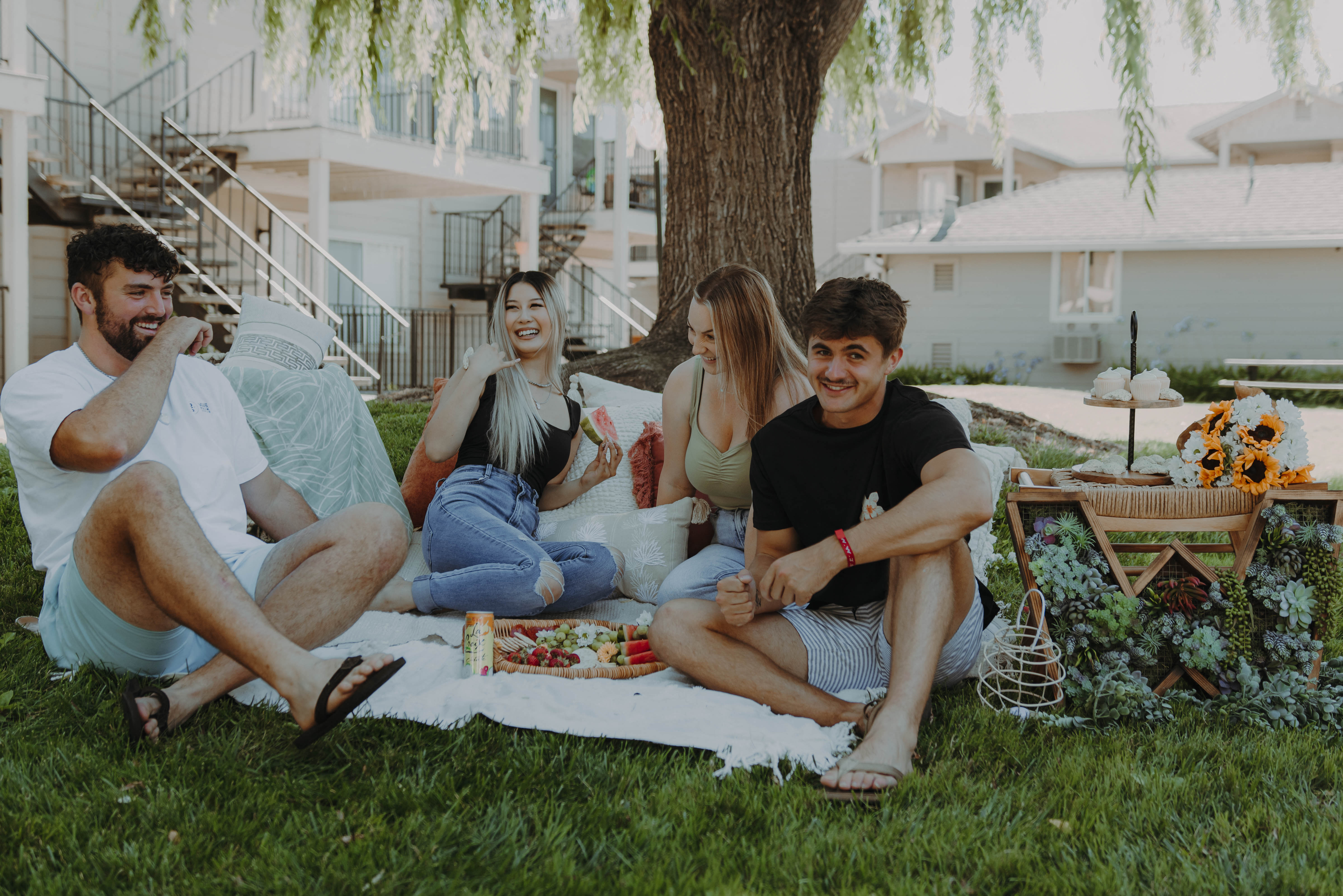 a group of friends sitting on a blanket under a tree