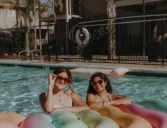 two women in a swimming pool wearing sunglasses and laying on inflatable rafts