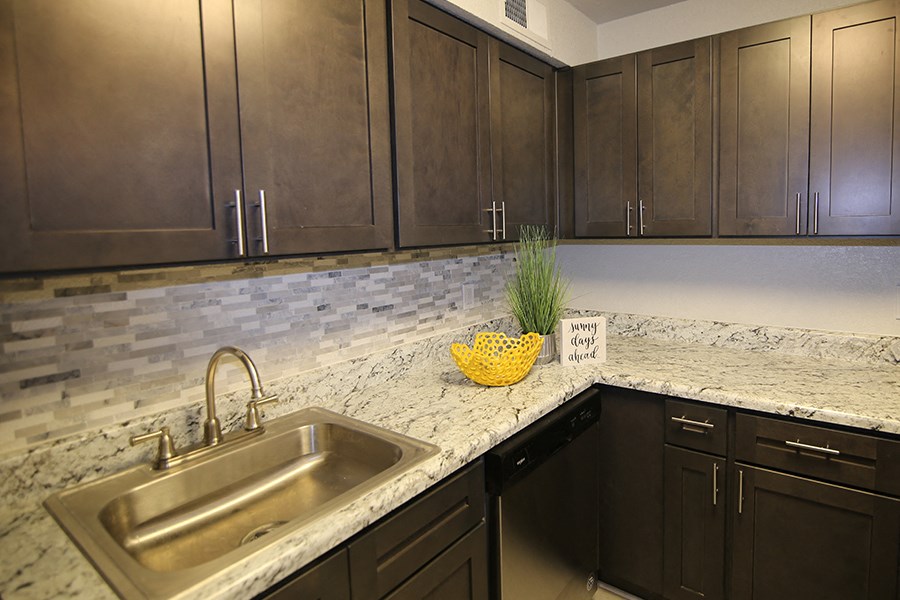 a kitchen with dark cabinets and a sink and marble counter top
