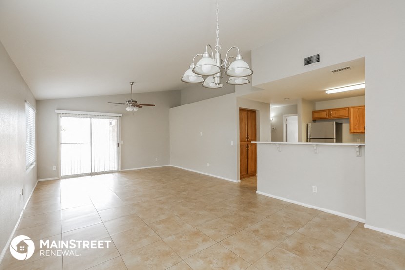an empty living room with a kitchen and a ceiling fan