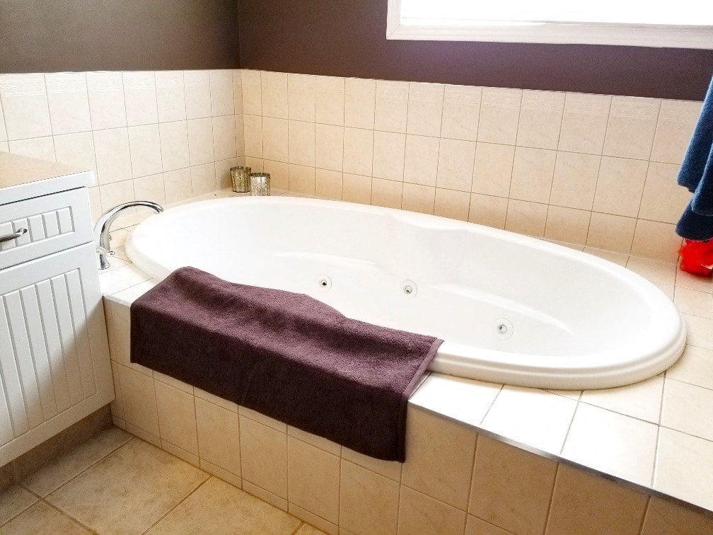 a large white bath tub in a white tiled bathroom