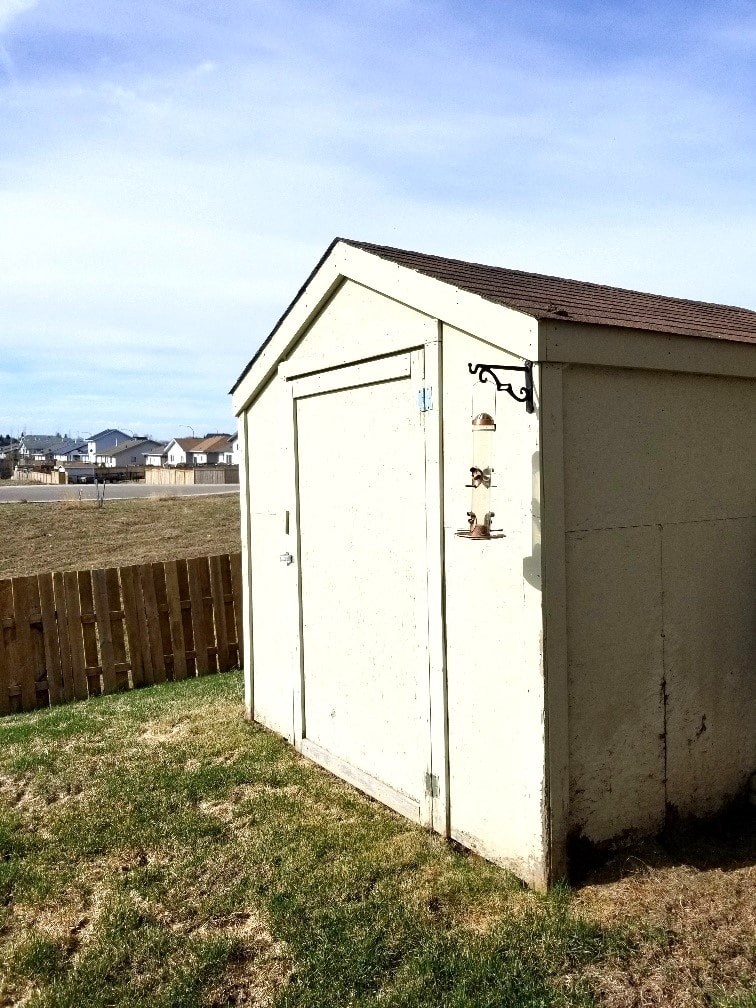 a small white shed in the grass next to a fence