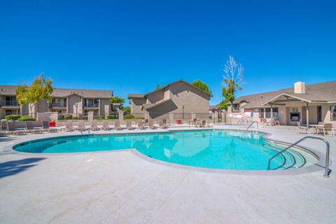 A large outdoor swimming pool surrounded by a concrete patio and residential buildings.