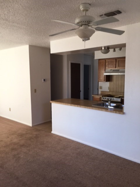 an empty living room with a kitchen and a ceiling fan