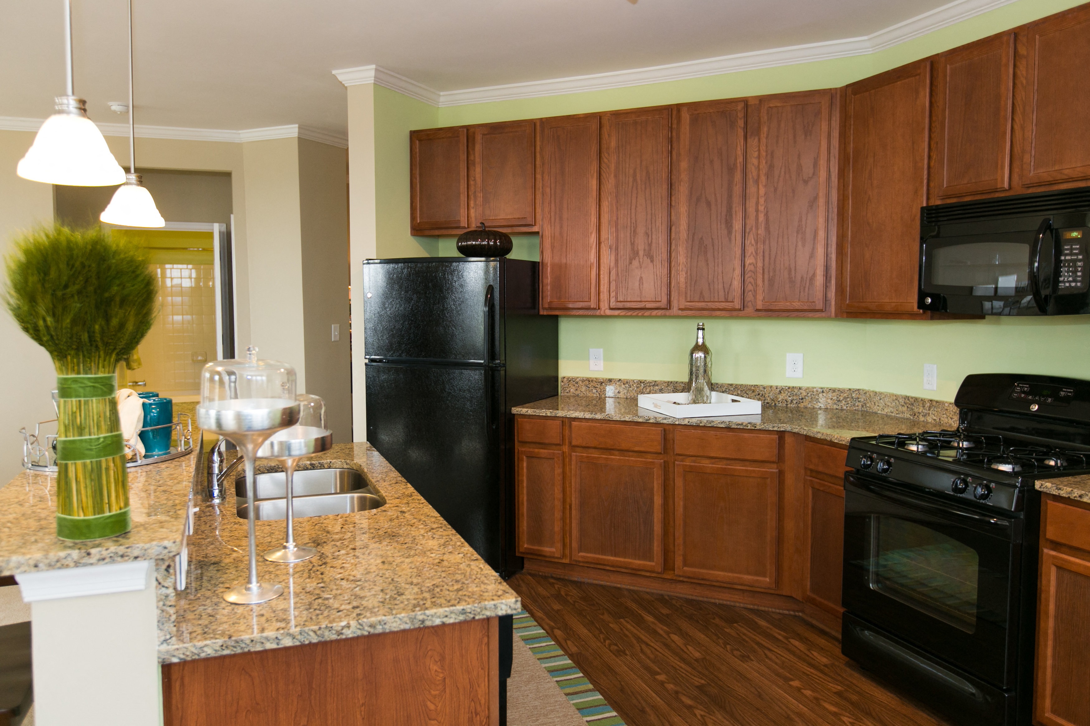 kitchen at VistaView apartments in Frederick, MD with black appliances, dark wood cabinets and flooring, kitchen island with sink and counter seating and stone countertops
