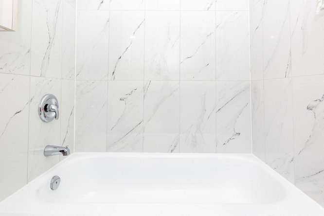 a white bath tub in a white tiled bathroom