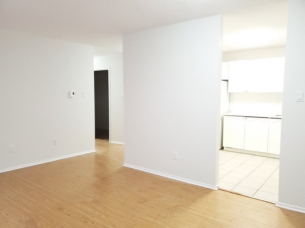 an empty living room and kitchen with white walls and wood floors