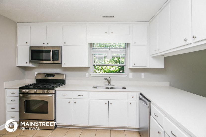 a white kitchen with white cabinets and stainless steel appliances and a window