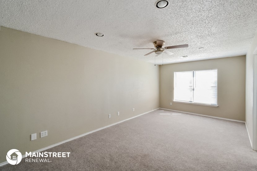 the spacious living room with ceiling fan and carpeting
