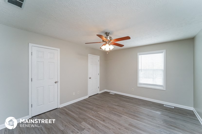 the spacious living room with ceiling fan and white door