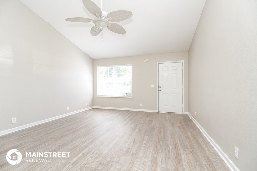 the spacious living room with wood flooring and a ceiling fan
