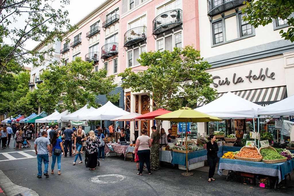 people walking around a farmers market in front of a building