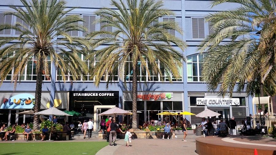 people walking outside of a shopping mall with palm trees