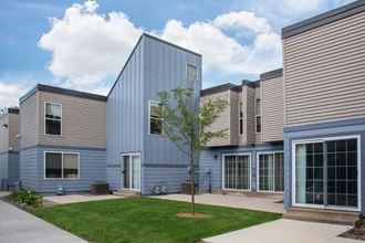 Photo of Albright Townhomes with patch of green grass, leafy tree and blue sky overhead with fluffy white clouds