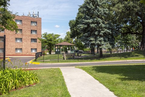 a sidewalk leading to a park with a gazebo and a brick building
