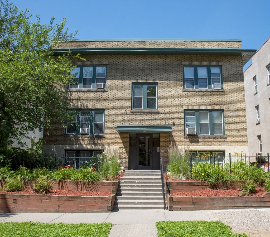 the front of a brick apartment building with stairs and a sidewalk