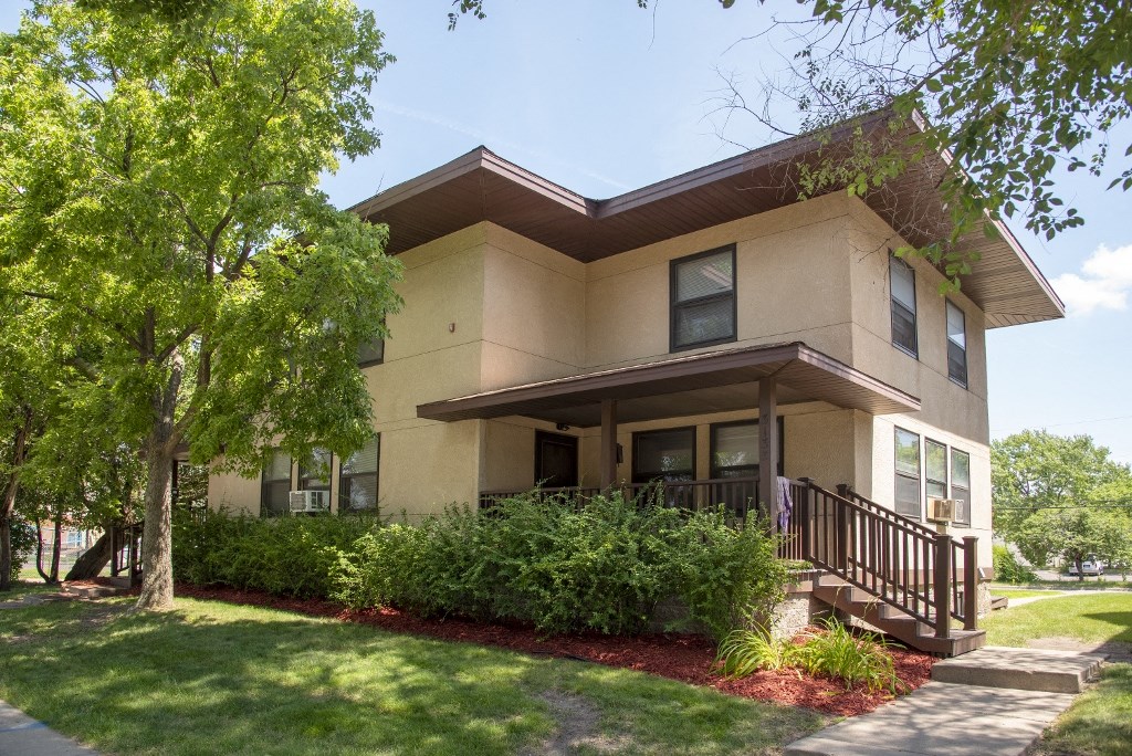 the exterior of a tan house with a front porch and trees