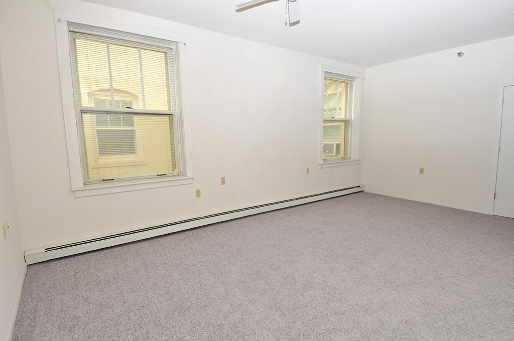 an empty bedroom with two windows and a carpeted floor