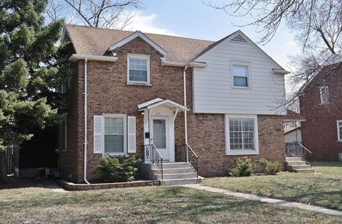 the front of a brick house with white siding and a lawn