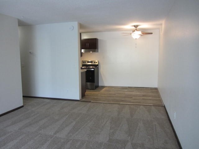 an empty living room with a kitchen and a ceiling fan