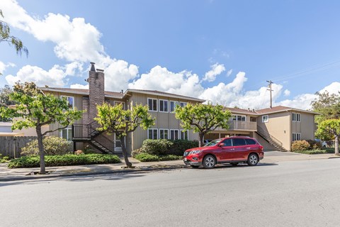 A red car is parked in front of a two-story apartment building.