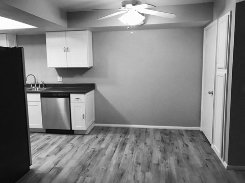 A kitchen with a black fridge, white cabinets, and a ceiling fan.