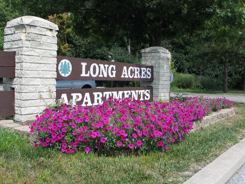 a sign for long acres apartments in front of a bed of flowers