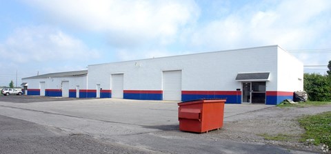A large white building with blue stripes and a red dumpster in front.