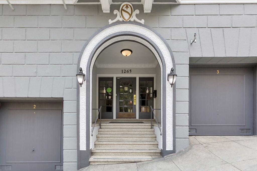 The entrance to a building with a grey facade and a large arched doorway.