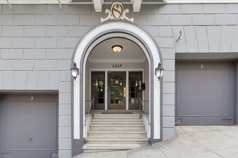 The entrance to a building with a grey facade and a large arched doorway.