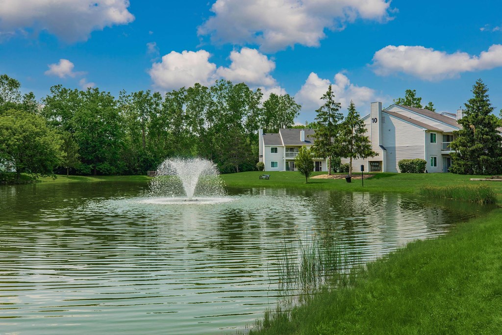 a fountain in the middle of a pond with a building in the background