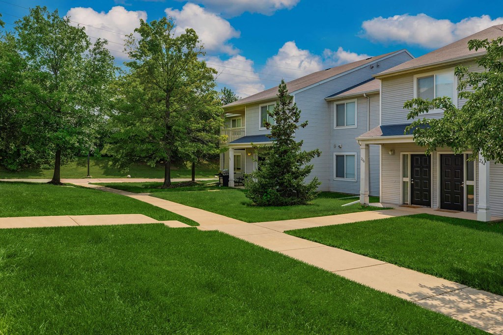 a sidewalk in front of a house with green grass and trees
