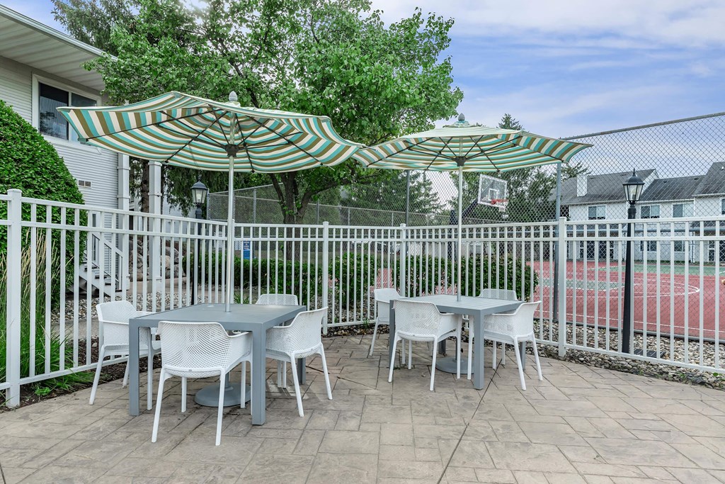 a patio with tables and umbrellas in front of a white fence