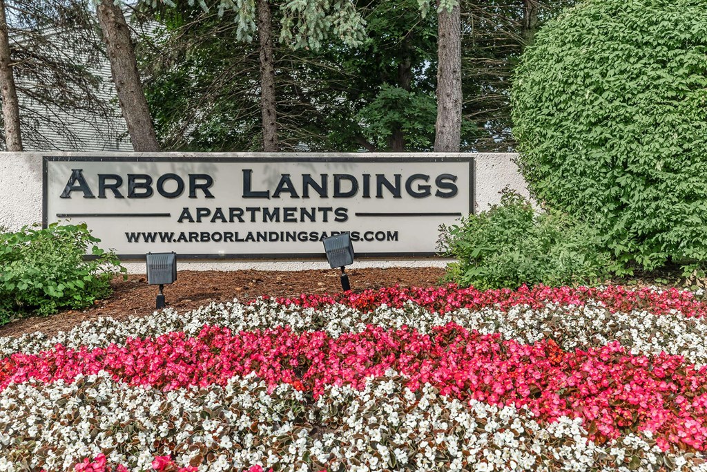 a sign for arbor landings apartments in front of a garden of flowers