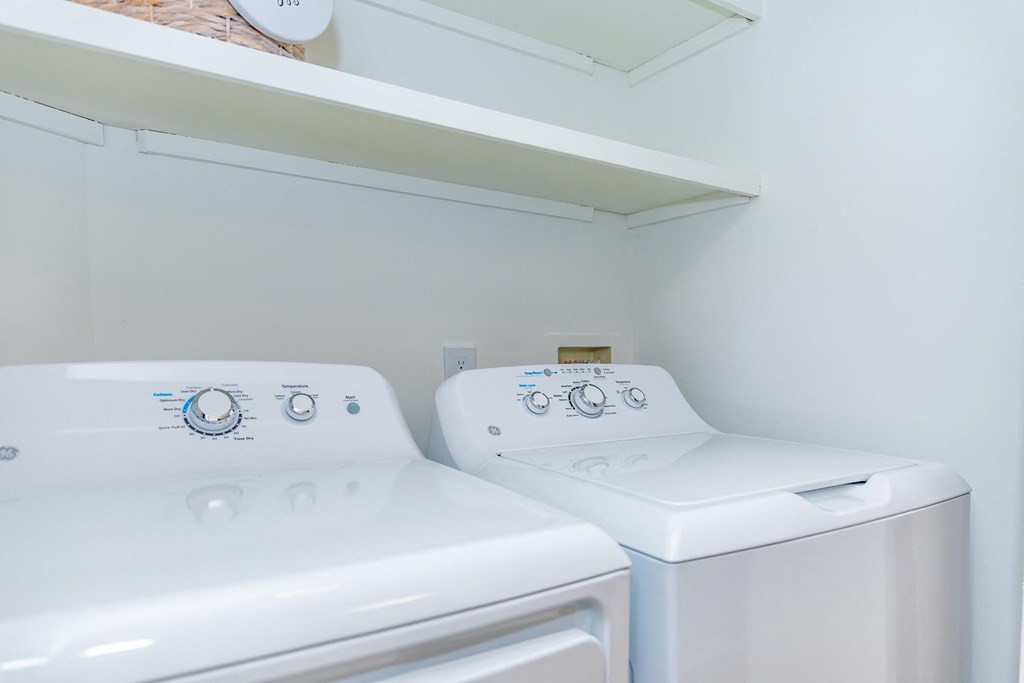 two washes and a dryer in a laundry room with a shelf above them