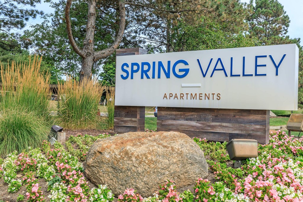a sign apartments with a rock and flowers