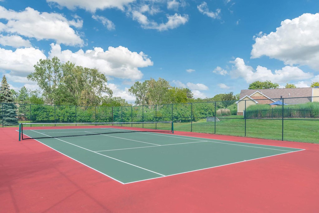 a tennis court with a fence and a house in the background