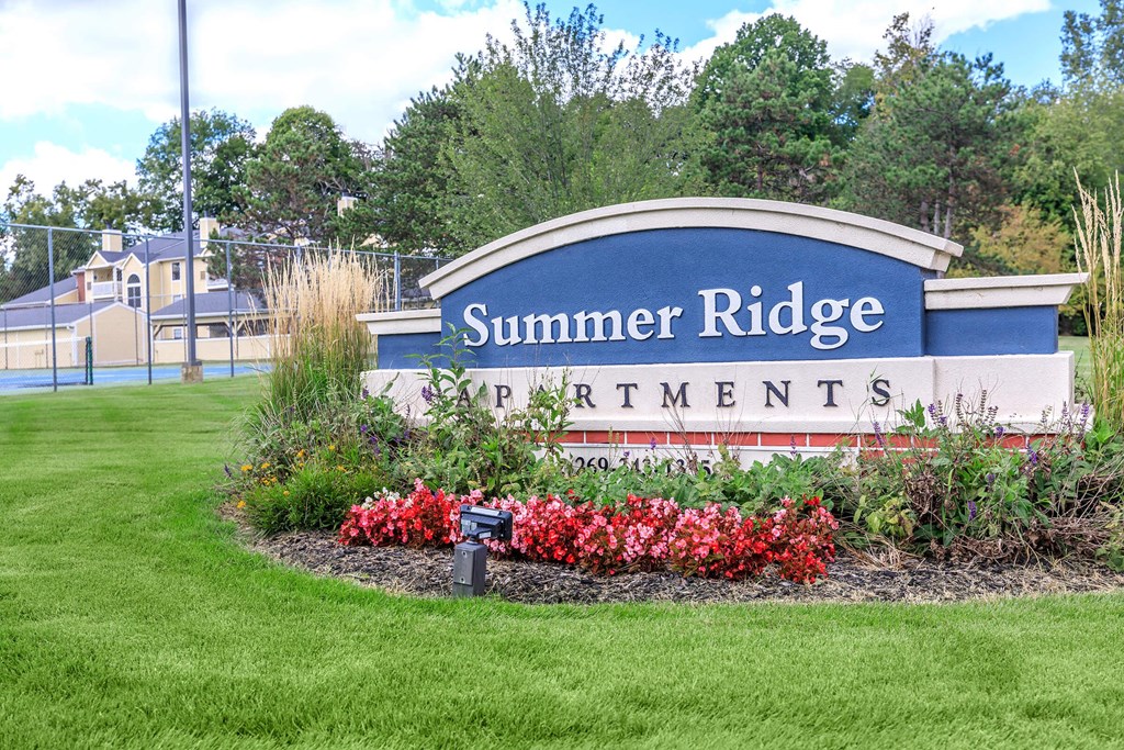 a sign for summer ridge apartments in front of a park with flowers