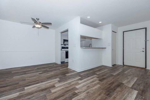 an empty living room with a ceiling fan and a kitchen