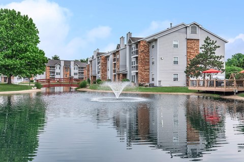 a fountain is in the middle of a pond with apartments in the background
