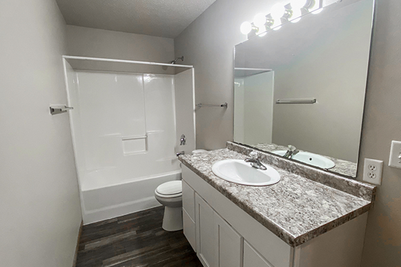 Modern bathroom with wood vinyl flooring, full shower, marble counter tops, and mirror