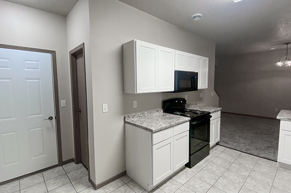 Garage access kitchen in Osgood Townhome with oven, microwave, closet, vinyl floor, cupboards, and marble counter tops